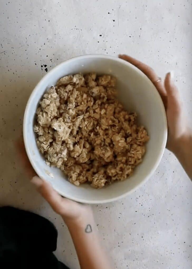 Hands holding a white bowl of crumble.
