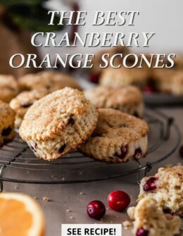 A side image of cranberry orange scones on a vintage cooling rack on a beige linen with more scones in the background and a halved orange and cranberries in the front.