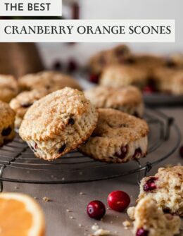 A side image of cranberry orange scones on a vintage cooling rack on a beige linen with more scones in the background and a halved orange and cranberries in the front.