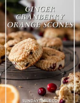 Two cranberry orange scones on a cooling rack with more scones and a gold pot in the background.