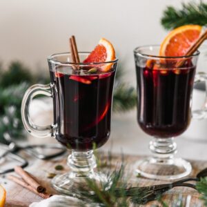 A closeup image of two mugs of glogg on a wood board next pine branches.