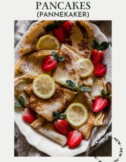 A very closeup image of Norwegian pancakes with berries, lemon, and mint on a white oval tray.