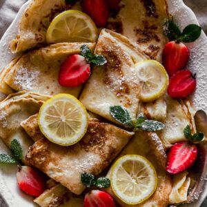 A super closeup image of Norwegian pancakes with strawberries, lemon slices, and mint leaves.