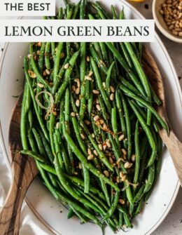A white dish of lemony green beans with pine nuts and garlic on a white counter.