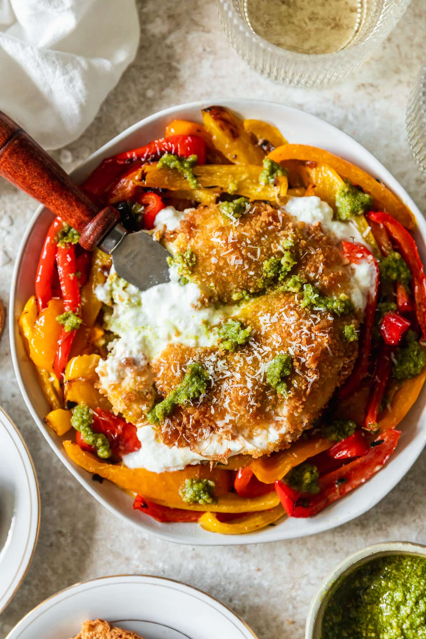 Fried burrata with roasted peppers and pesto on a white plate next to white wine and crackers on a beige counter.