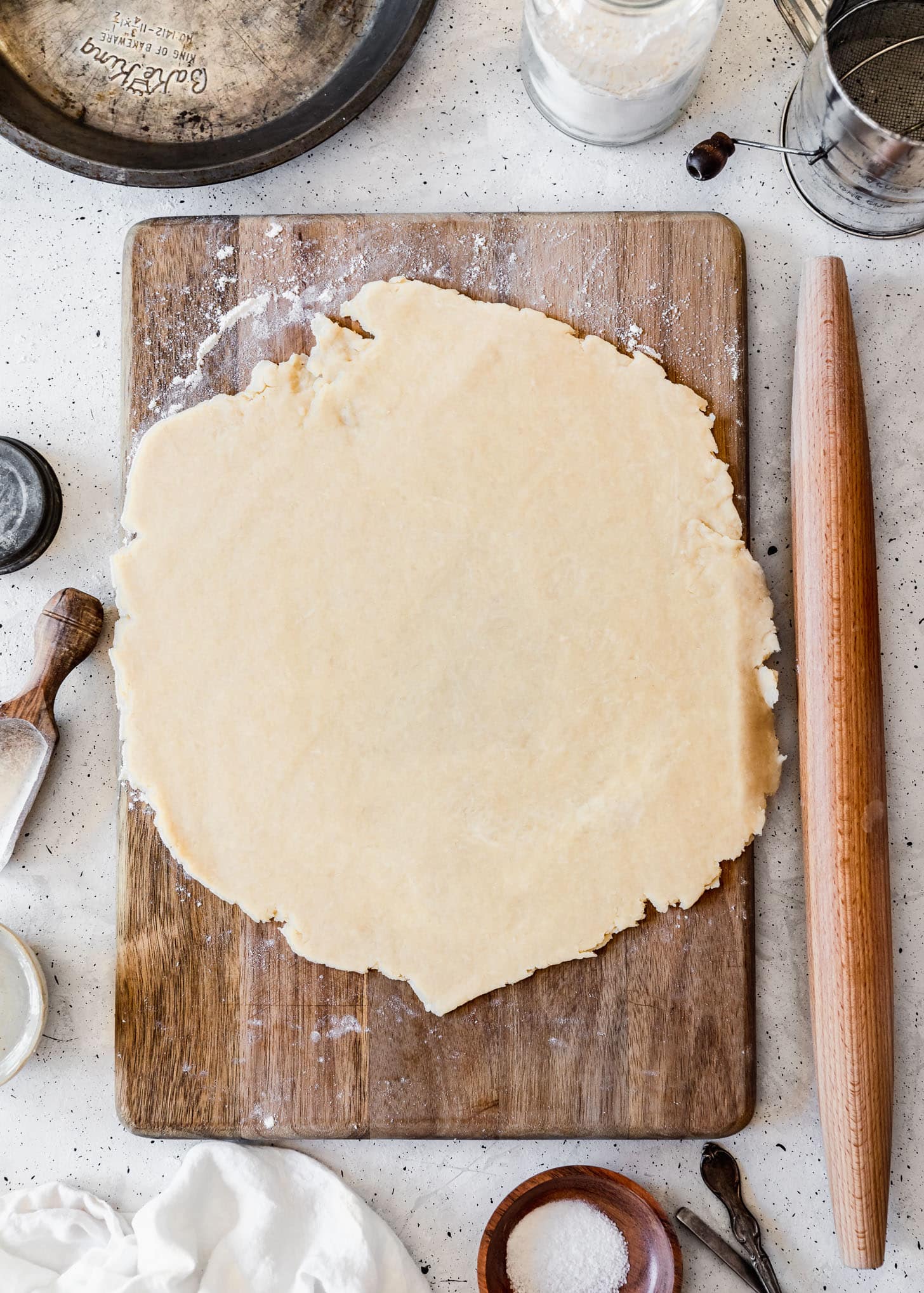 The best pie crust rolled out on a wood board next to baking tools and ingredients with a grey background.