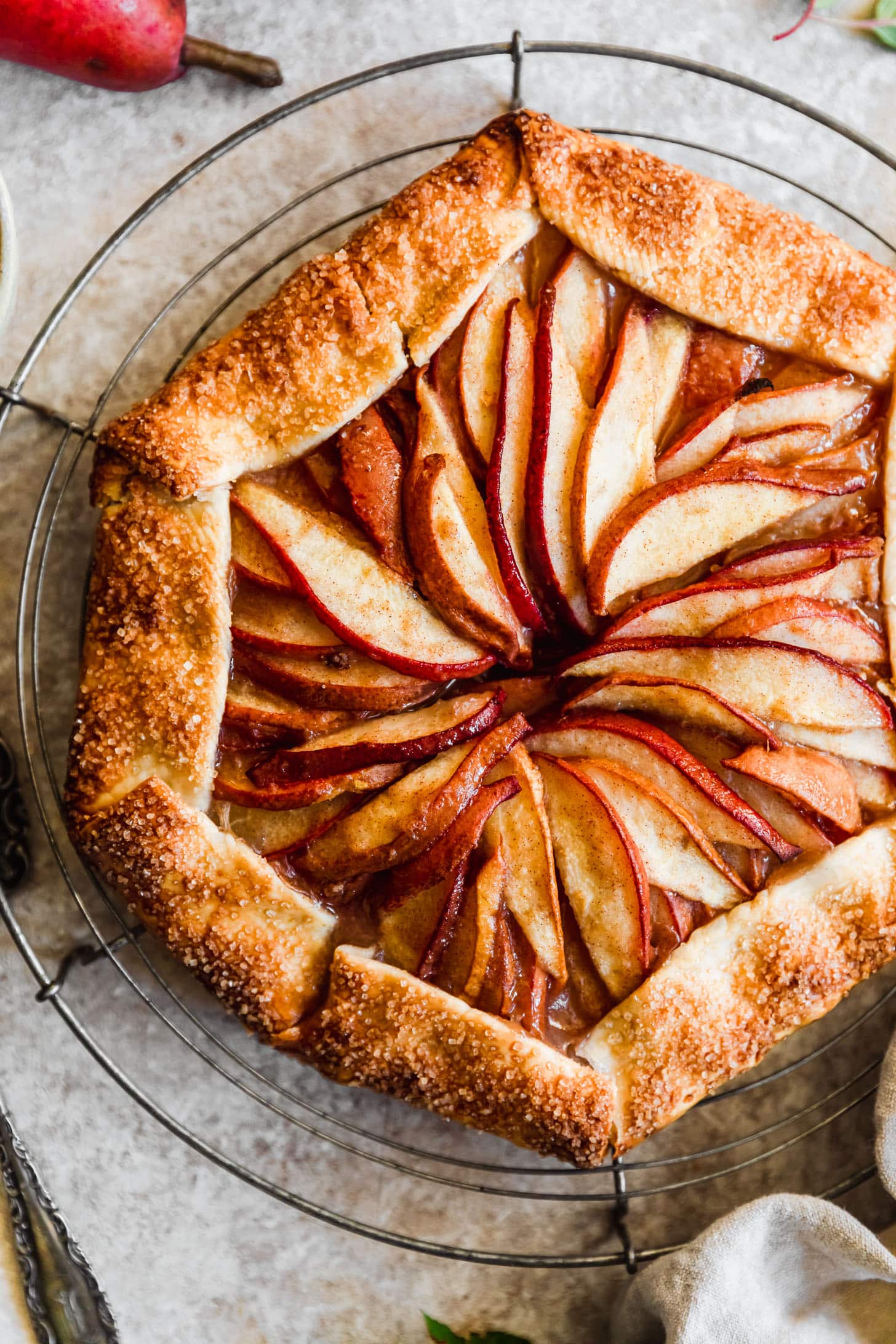 A close up of a ginger pear galette on a wire rack with a tan background.