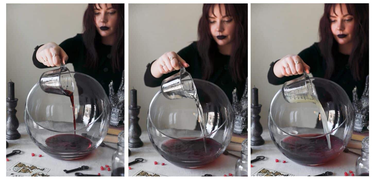 Three images making witches brew cocktail punch. In photo 1, a woman dressed as a witch is pouring blueberry liqueur into a punch bowl on a white counter next to black candles, Halloween decorations, and tarot cards. In photo 2, she's adding tequila to the bowl. In photo 3, she's adding lemon juice.