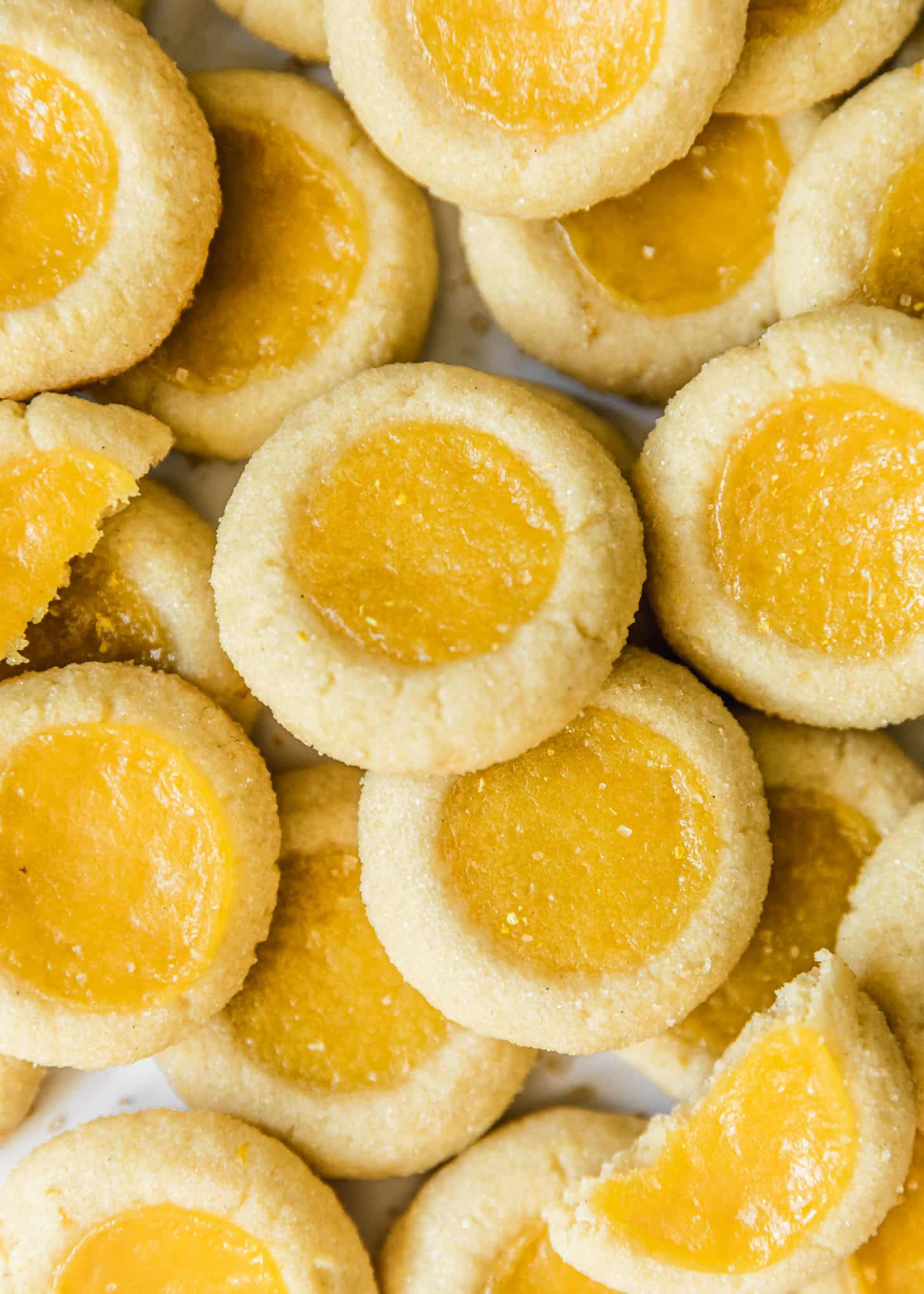 Piles of thumbprint lemon curd cookies on a white background.