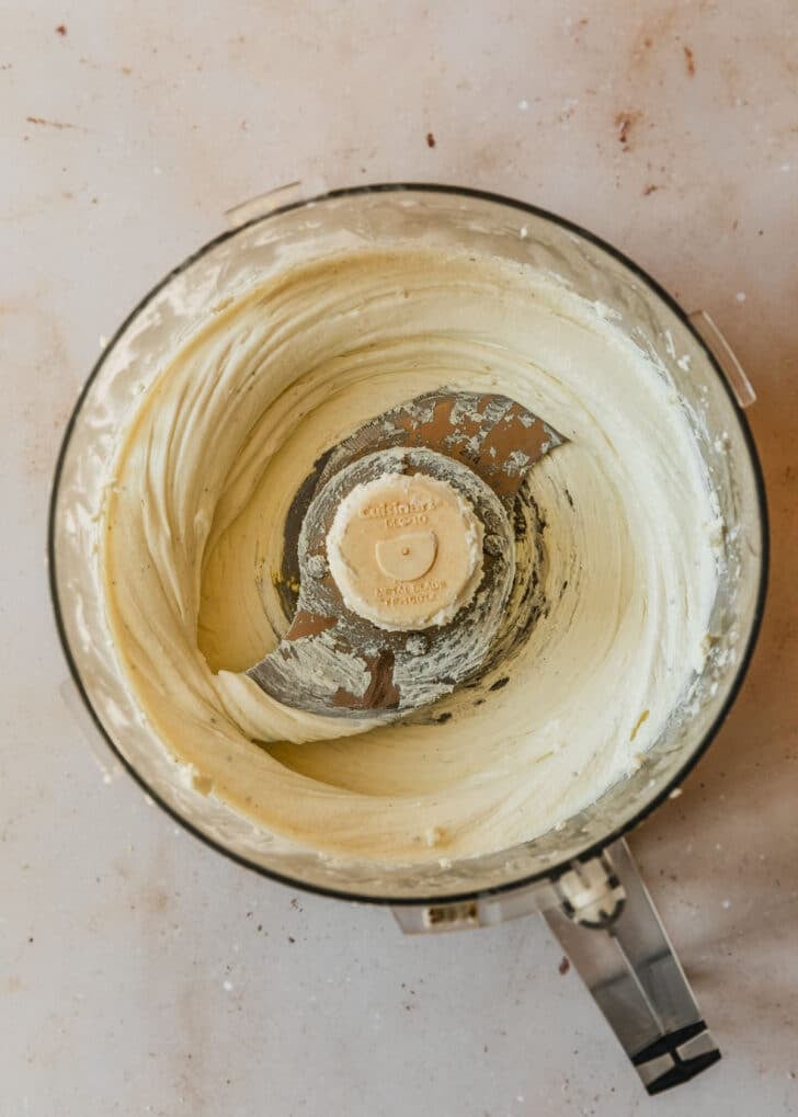 Blended cheese in a food processor on a tan counter.