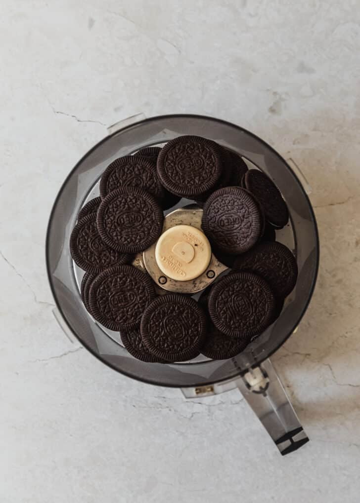 Chocolate cookies in a food processor on a white marble counter.