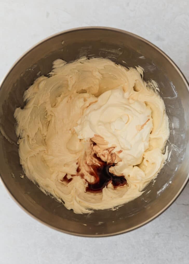 A silver bowl with cream cheese, sour cream, and vanilla on a white counter.