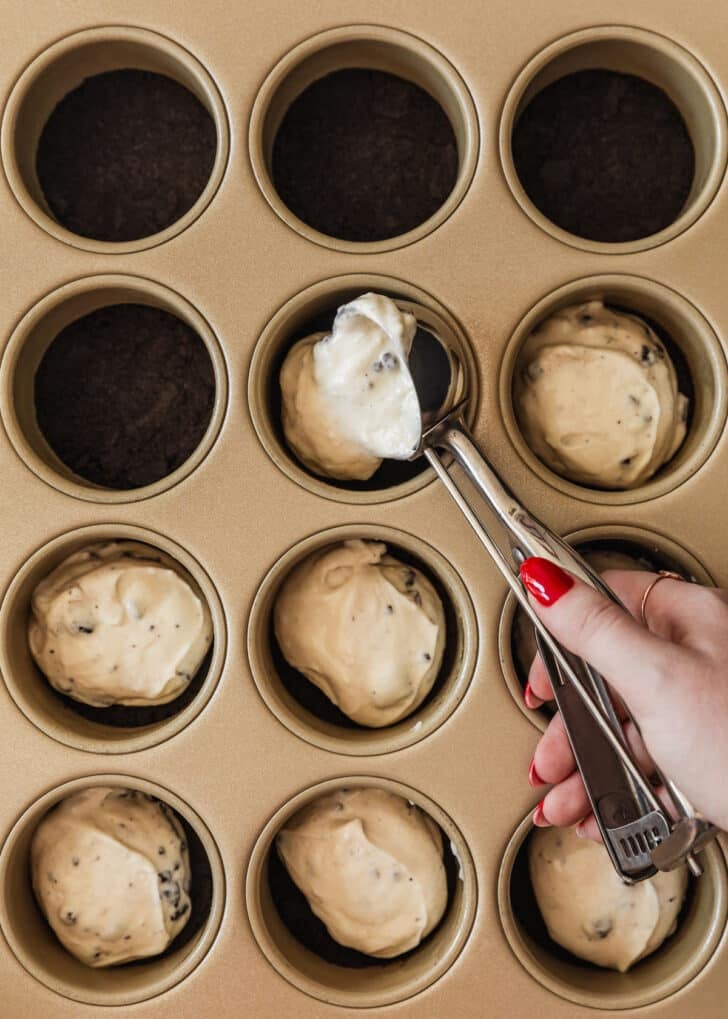 A hand scooping Oreo filling into a mini cheesecakes pan.