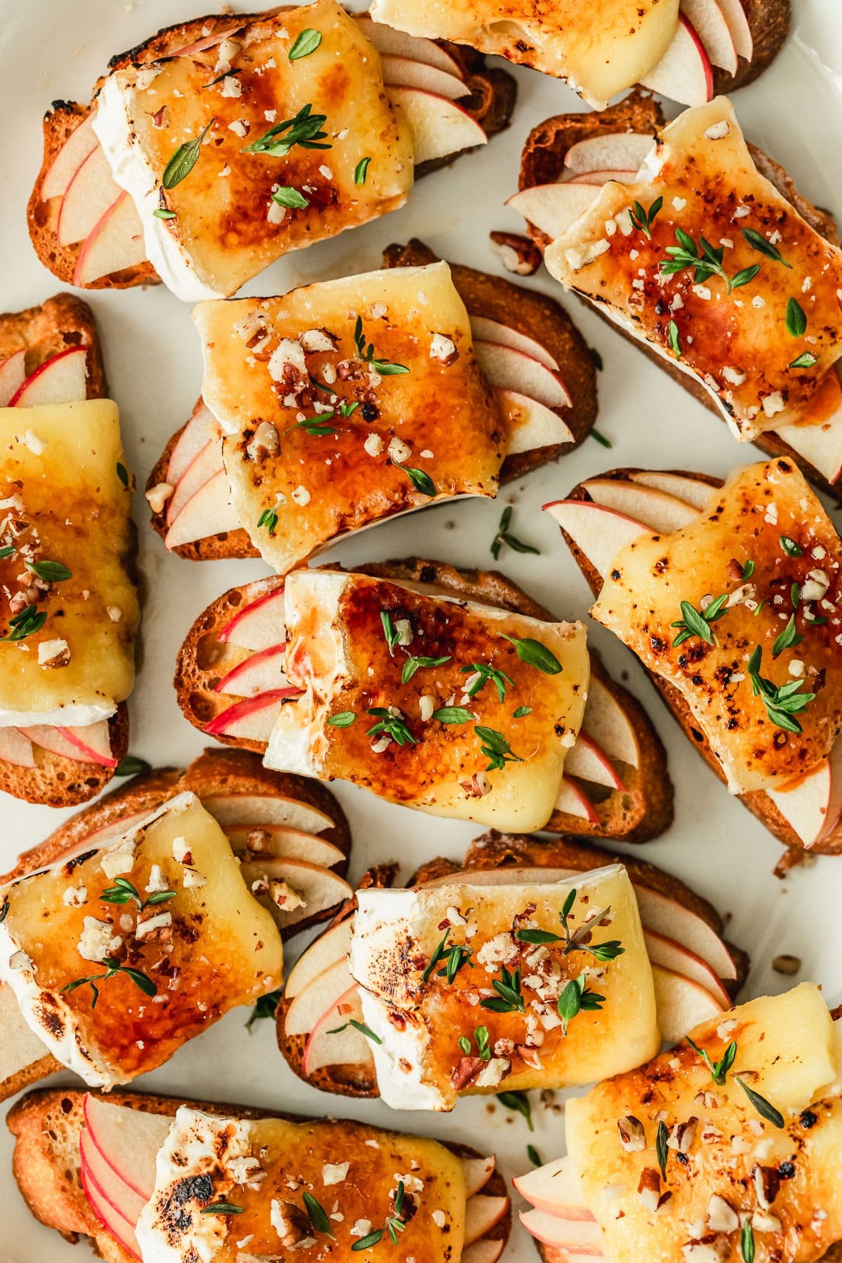 Rows of brûléed apple and brie crostini on a white plate.