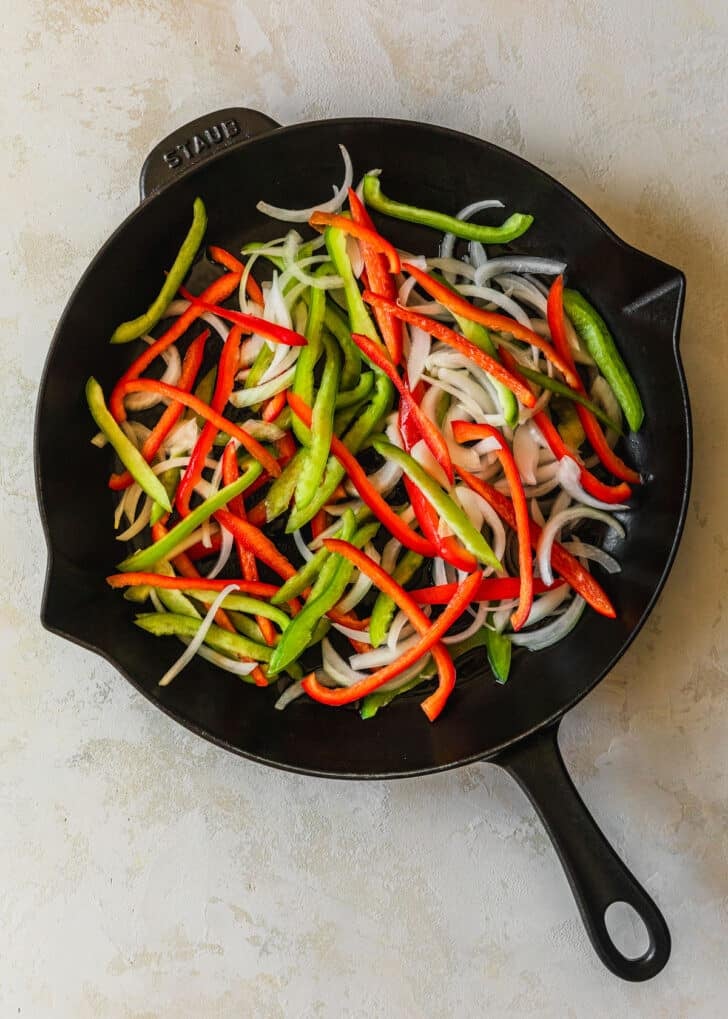 A cast iron skillet with peppers and onions on a tan counter.