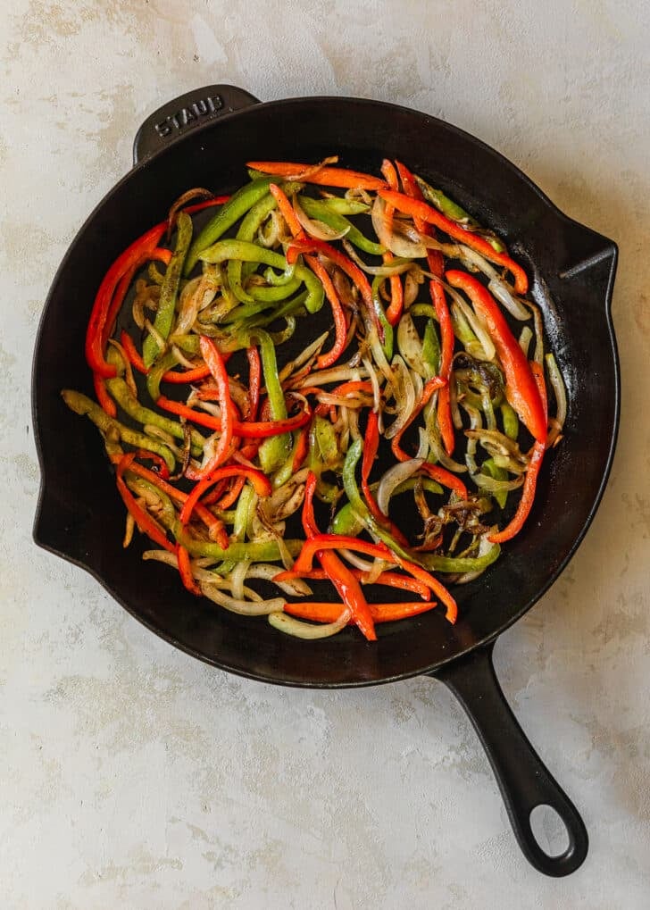 Sautéed peppers and onions in a cast iron skillet on a tan counter.