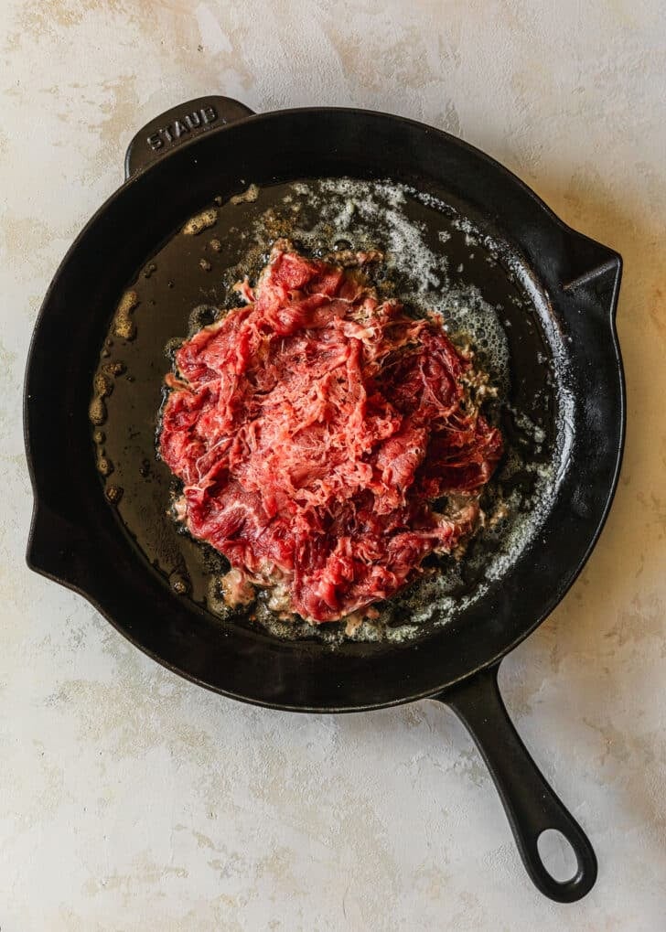 Steak in a cast iron skillet on a tan counter.