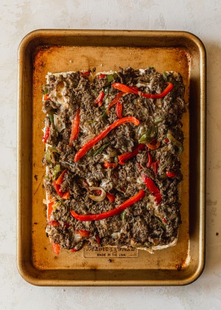 Hawaiian rolls topped with Philly cheesesteak filling on a gold sheet pan.