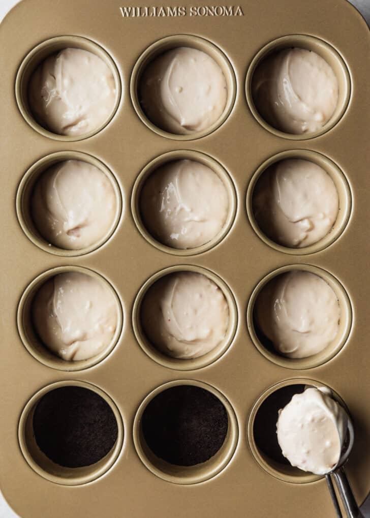 Peppermint bark cheesecake filling being scooped into a mini cheesecakes pan.