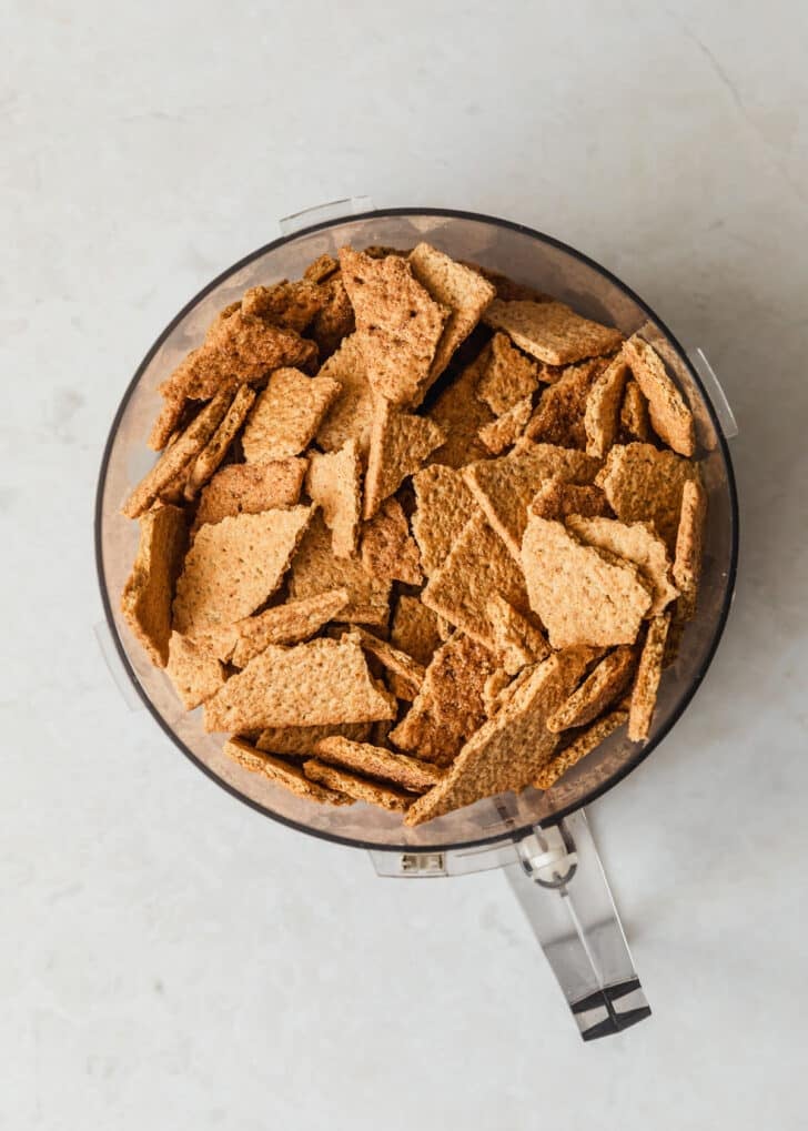 A food processor with graham crackers on a white counter.