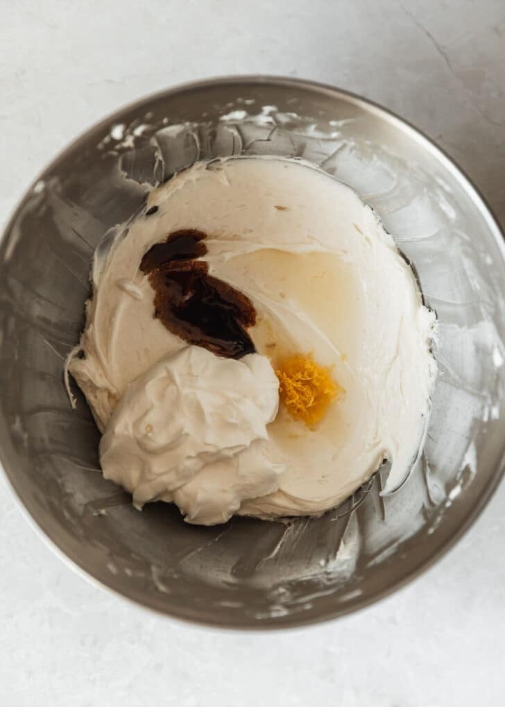 A silver bowl with cream cheese, sugar, sour cream, vanilla, and lemon on a white counter.