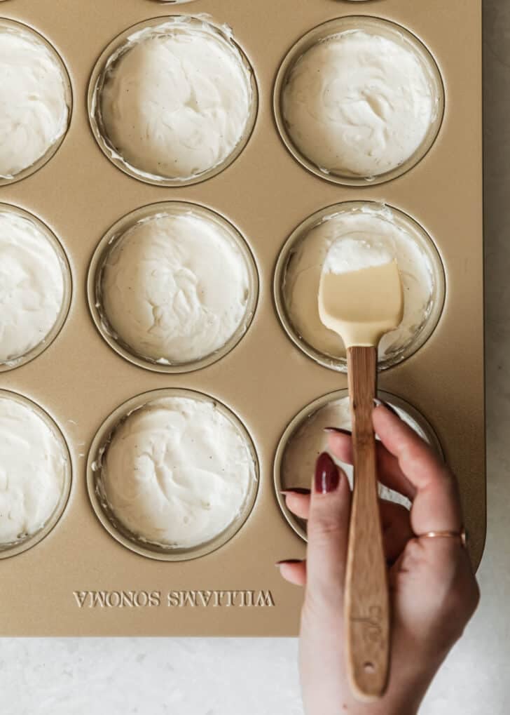 A hand smoothing no-bake filling in a mini cheesecake pan.