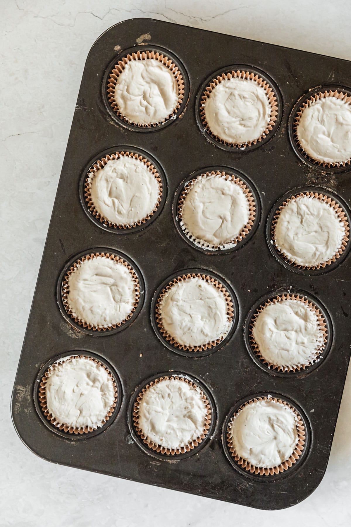 A cupcake pan with mini no bake cheesecakes on a marble counter.