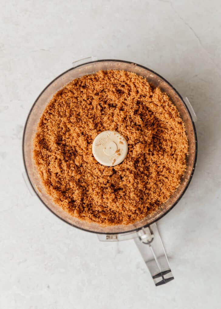 A food processor with graham cracker crust on a white counter.