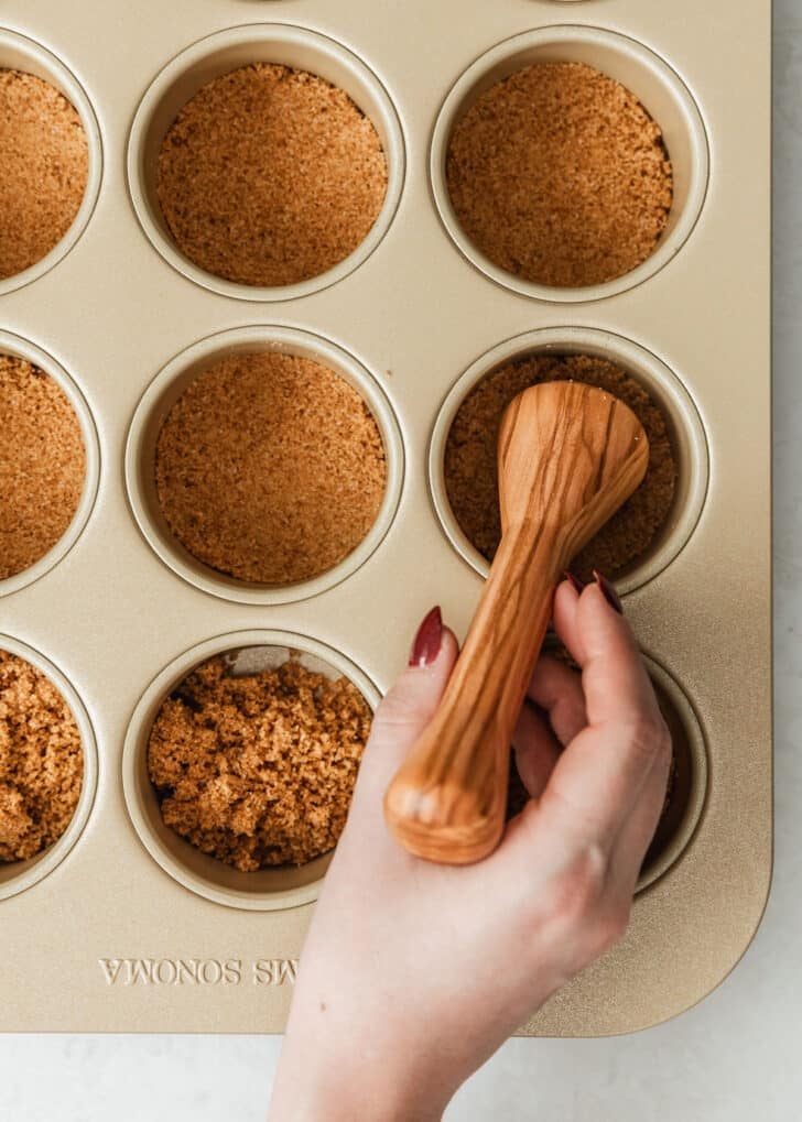 A hand using a pastry tamper to press crust into mini pans.