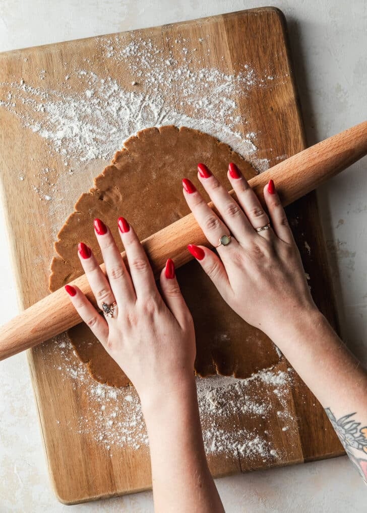 Hands using a rolling pin to roll out gingerbread dough.