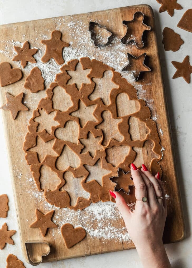 A hand using mini cookie cutters to cut out gingerbread dough.