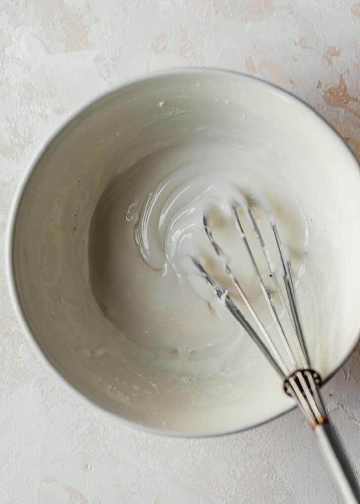 A white bowl of maple icing on a beige counter.