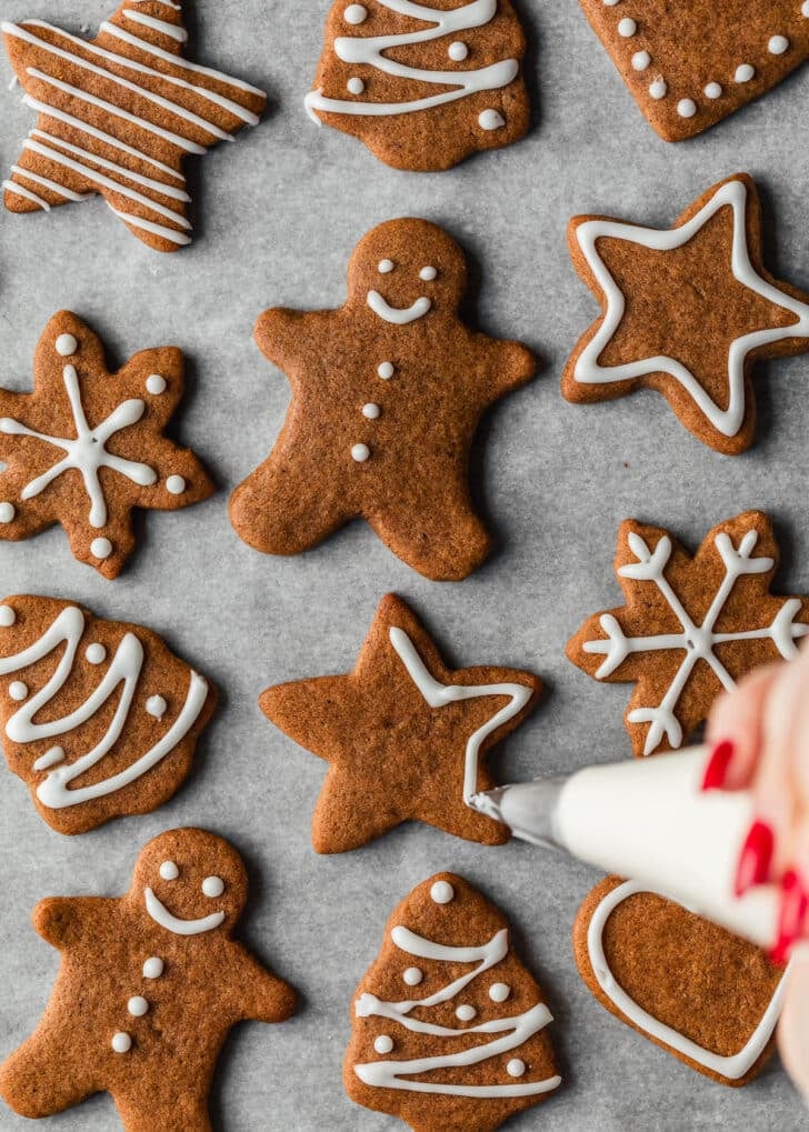 A hand using a piping bag to decorate mini gingerbread cookies.