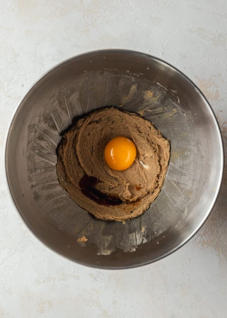 A silver bowl with whipped butter and brown sugar topped with an egg and vanilla on a beige counter.