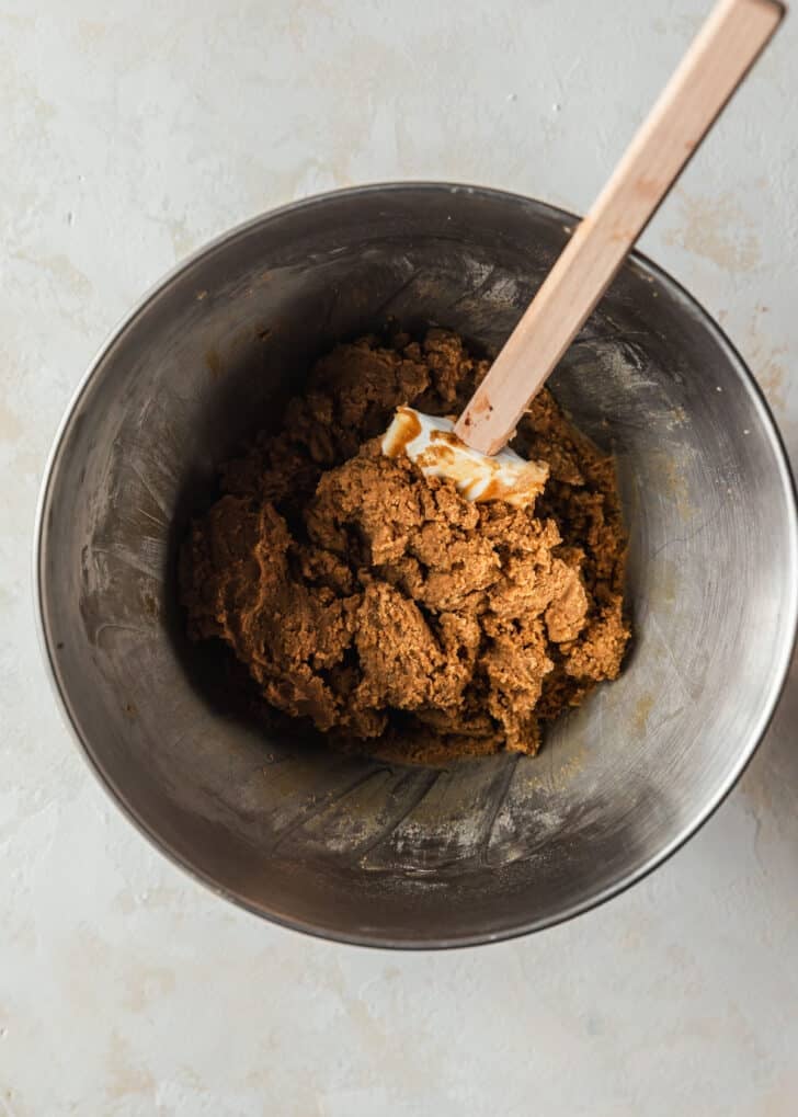 A silver bowl of mini gingerbread cookies dough with a rubber spatula on a tan counter.