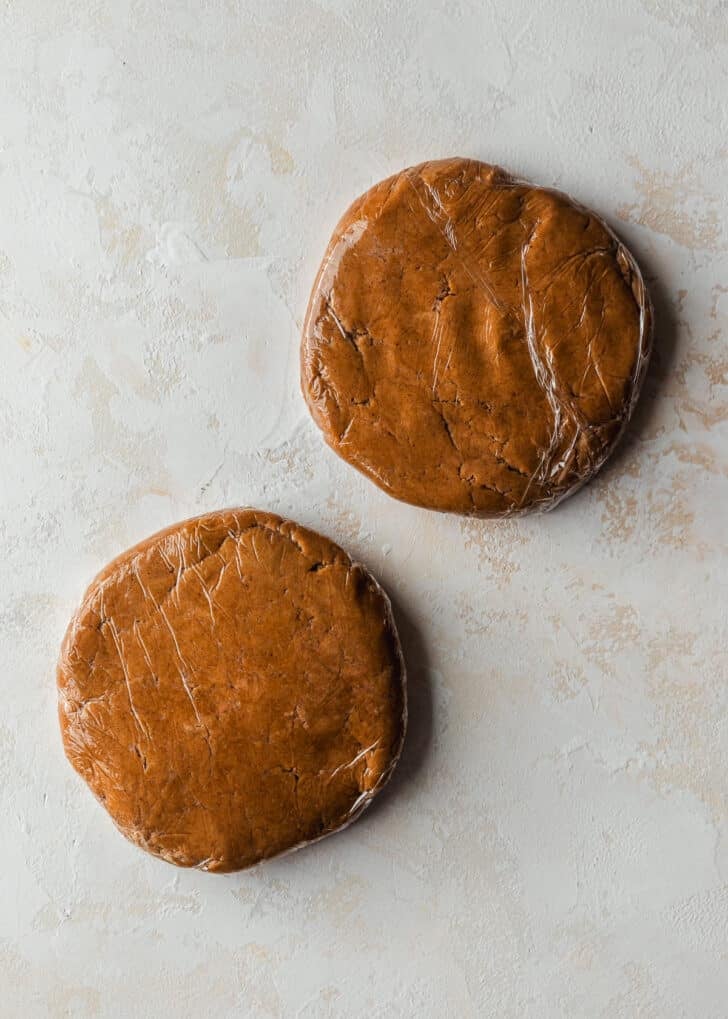 Two discs of mini gingerbread cookies dough on a beige table.