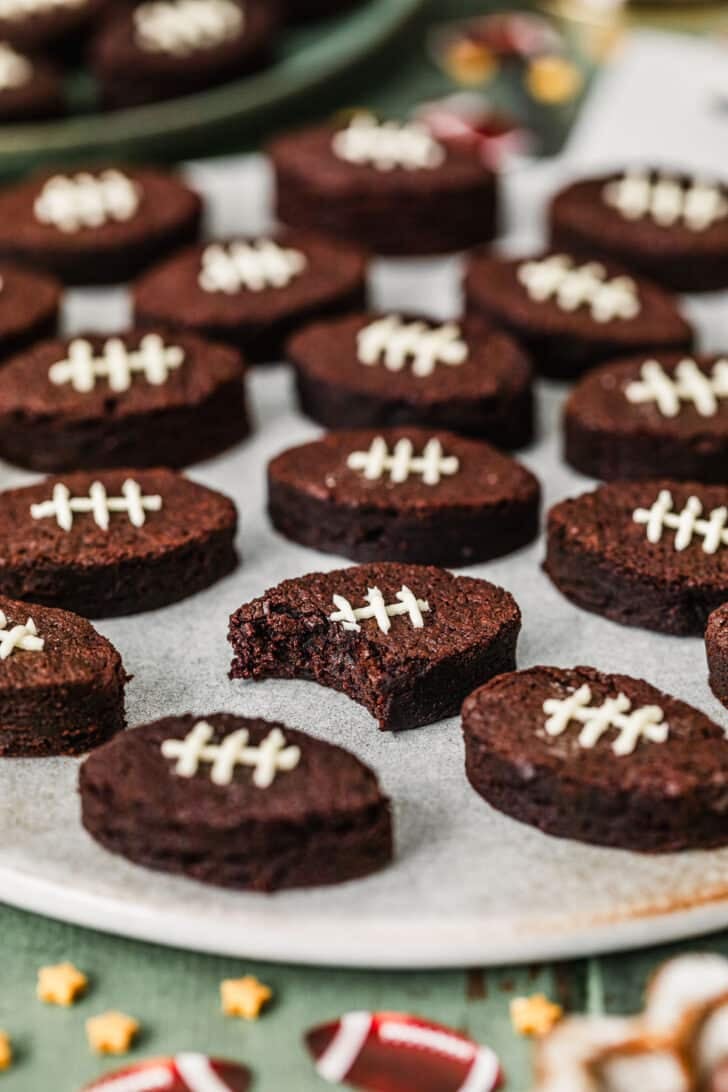 A brownie with a bite taken out of it on a grey platter next to mini football brownies, a green plate, and football confetti on a green table.