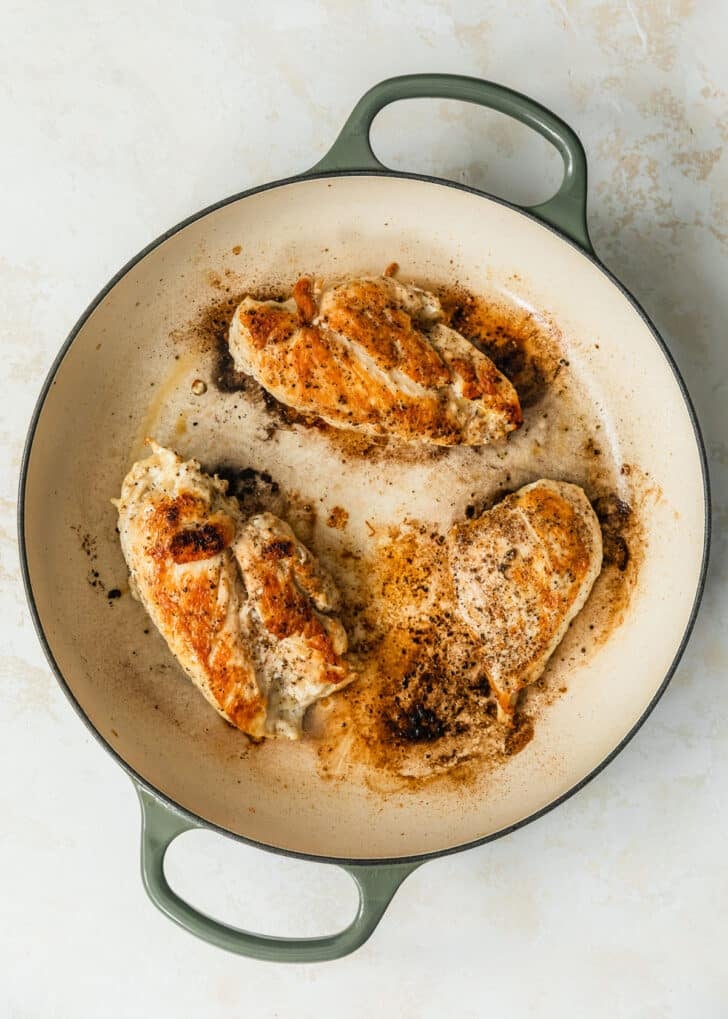 A Dutch oven with seared chicken on a tan counter.