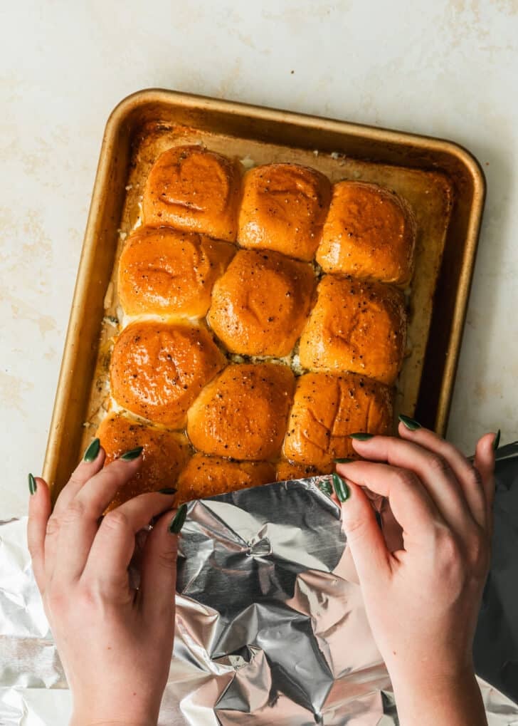 Hands covering a pan of buffalo chicken sliders with foil.