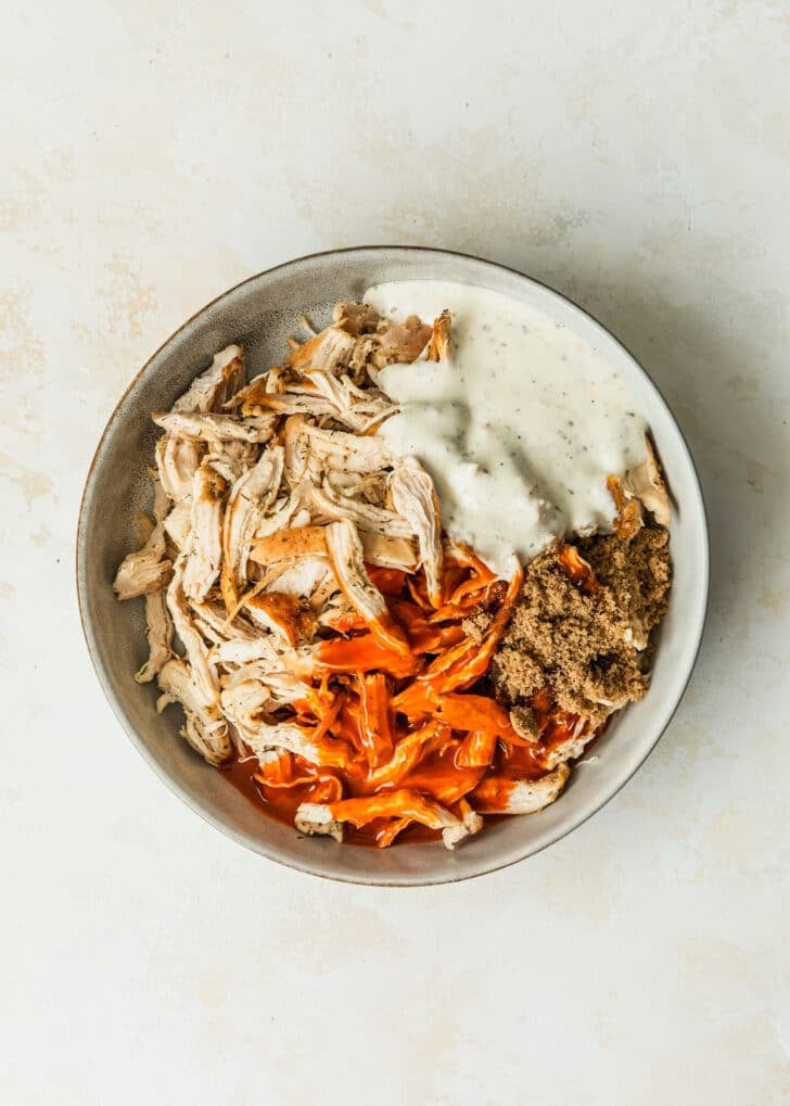 A grey bowl of chicken, ranch, buffalo sauce, and brown sugar on a tan counter.