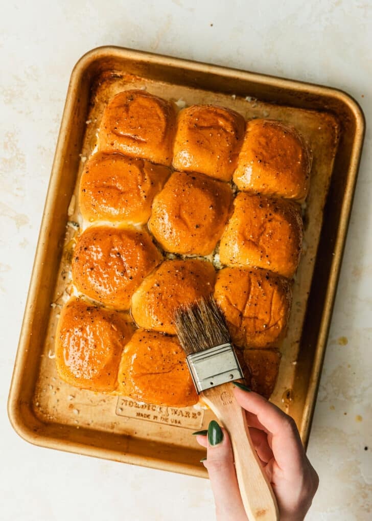 A hand using a pastry brush to brush butter over buffalo chicken sliders.