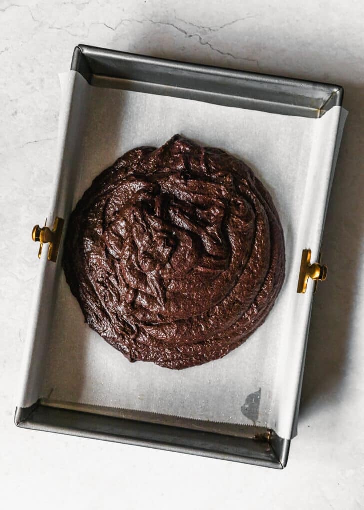 A silver pan with parchment and brownie batter on a white counter.