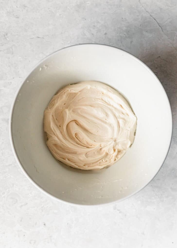 A white bowl of vanilla buttercream on a marble counter.