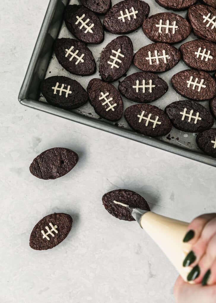 A hand using a piping bag to pipe lines on mini football brownies.