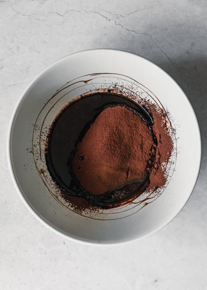 A white bowl with melted chocolate and cocoa powder on a marble counter.