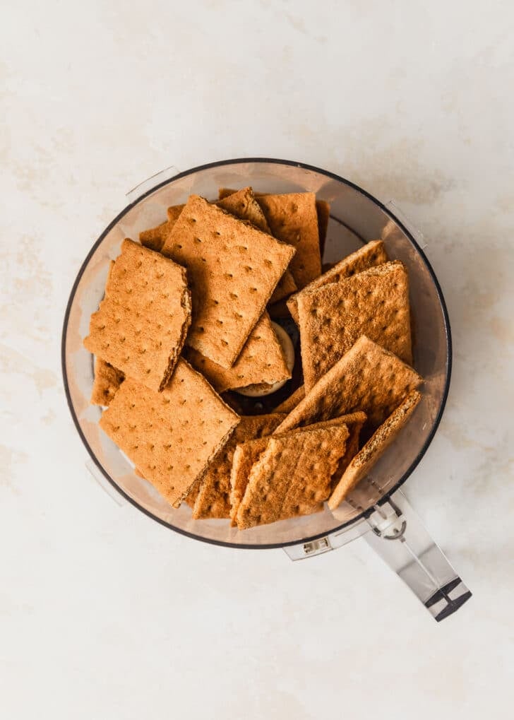 A food processor with graham crackers on a tan counter.