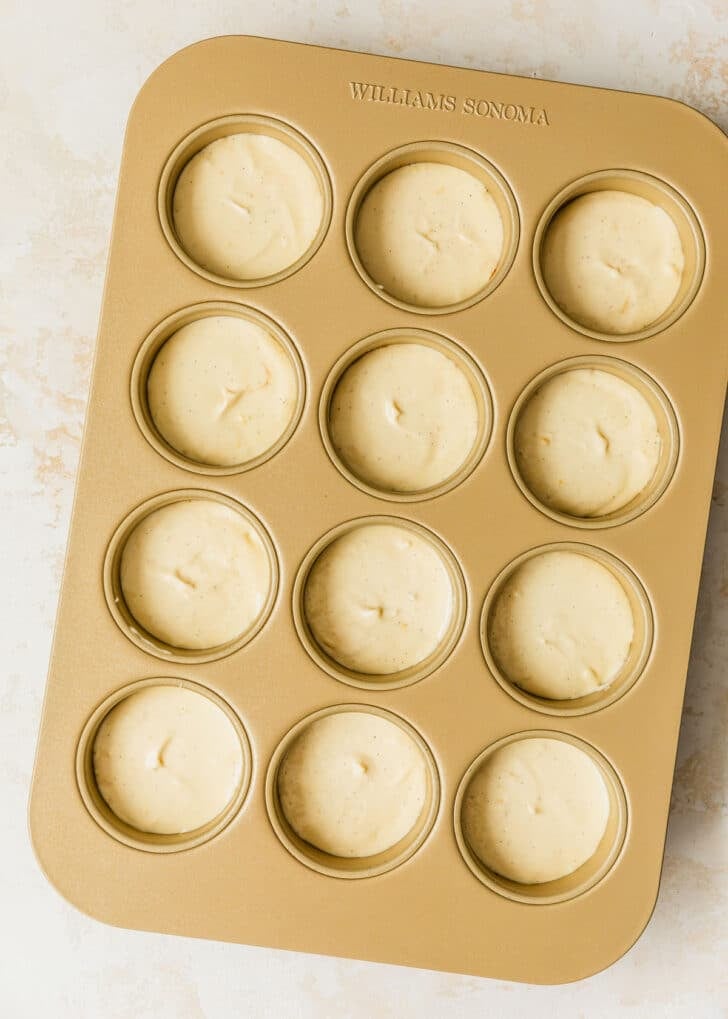 A mini cheesecake pan of raw cheesecakes on a tan counter.