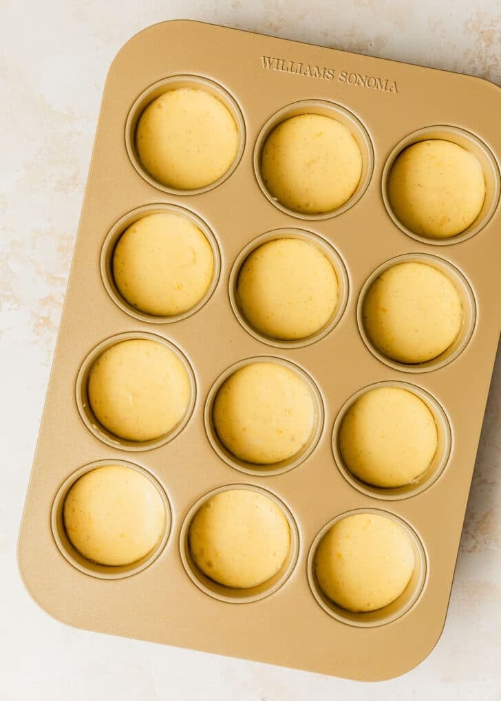 A gold pan of mini strawberry cheesecakes on a tan counter.