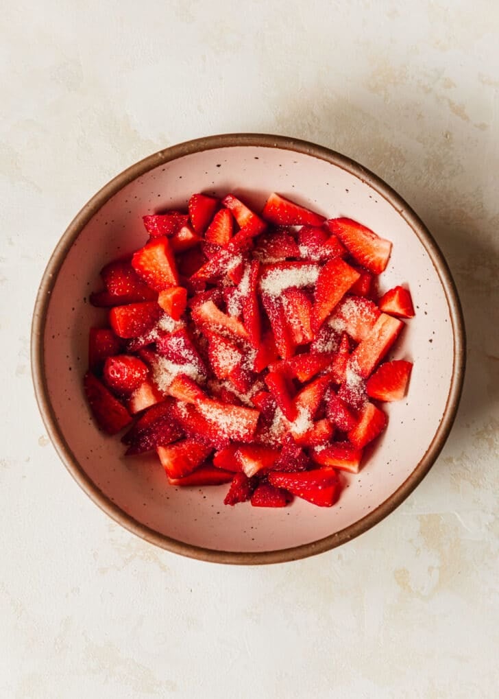 A pink bowl of strawberries on a tan counter.