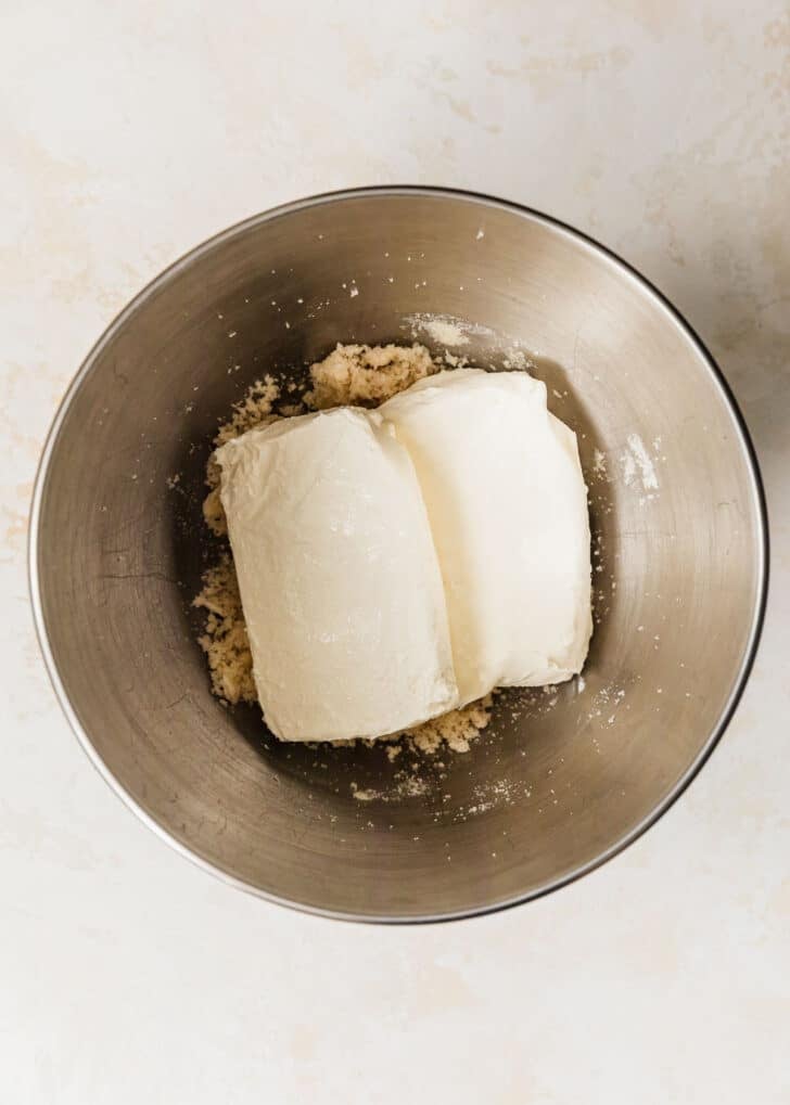 A silver bowl of butter, sugar, and cream cheese on a beige stone backdrop.